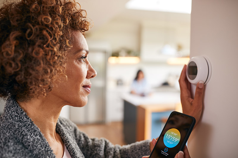 Woman using smart phone to control thermostat