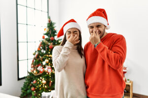 Couple standing by Christmas tree pinching their noses