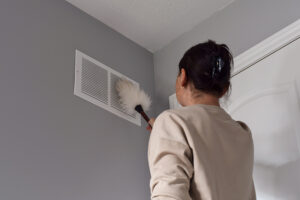 Woman cleaning an air vent with duster.