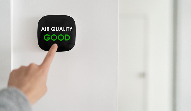 Hand touching smart thermostat showing good air quality.