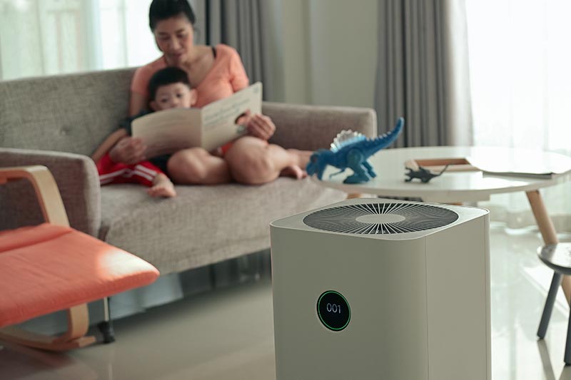 Mother and child sitting on couch beside a home air purifier.