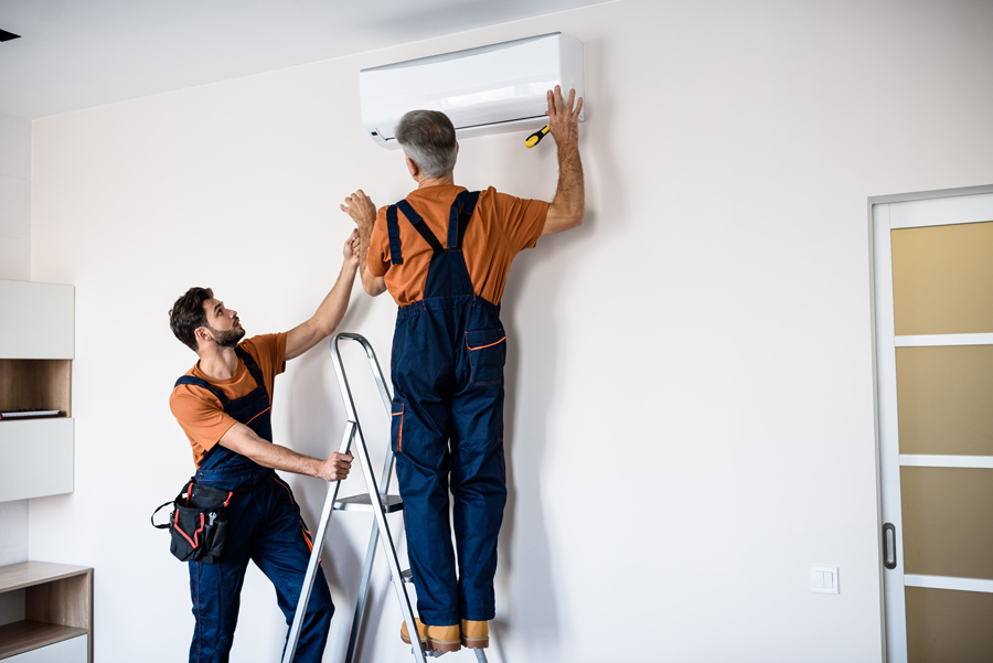 Two technicians installing a wall-mounted air conditioner unit indoors