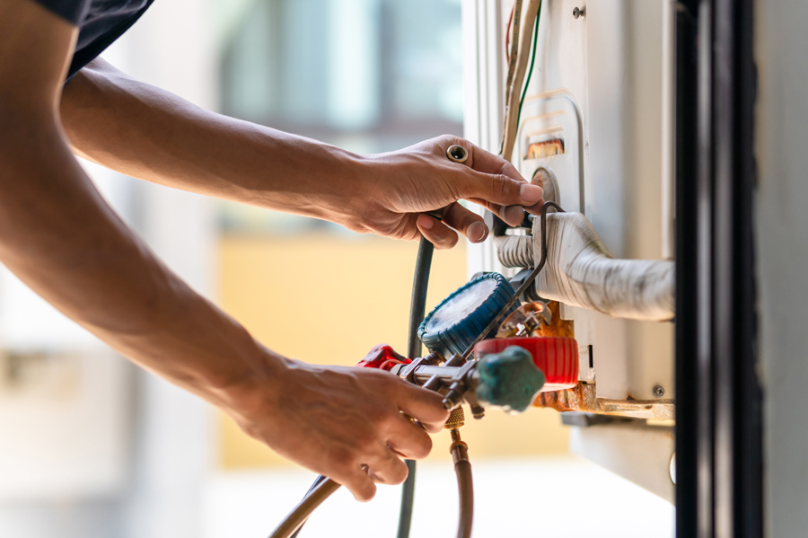 A person’s hands are adjusting gauges and wires on an air conditioning unit, performing maintenance or repair work.