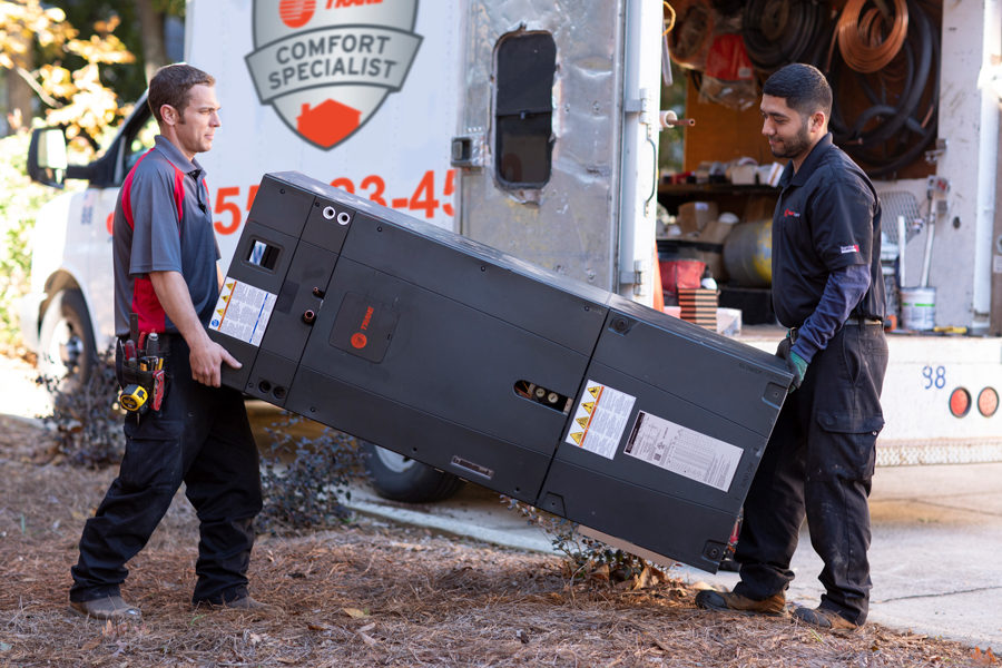 Two technicians carry Trane HVAC unit.